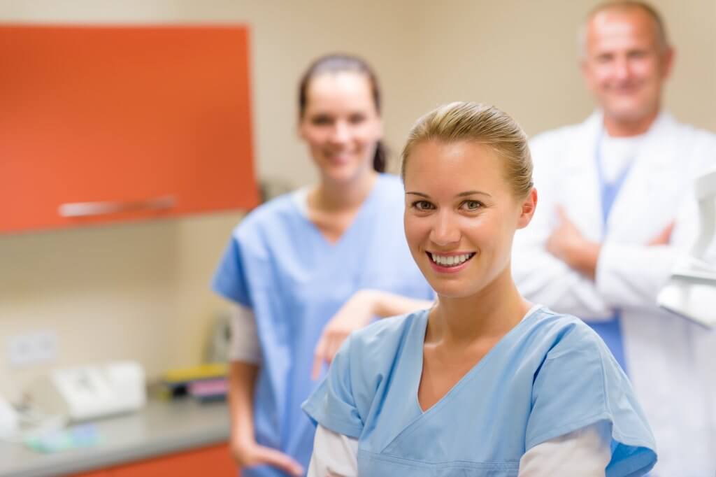 Medizin Angestellte im Vordergrund, während im Hintergrund eine andere Medizin Angestellte und ein Arzt lächeln.